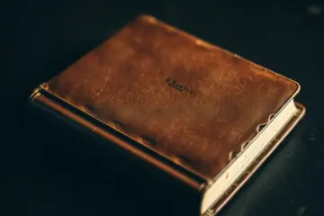 alt_text: A close-up, weathered brown leather book cover rests on dark wood, highlighted by soft, dramatic side lighting.