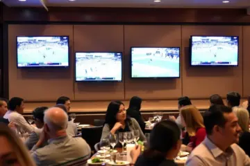 alt_text: A lively upscale restaurant with guests watching various sports on sleek, wall-mounted TVs during a bustling dinner service.