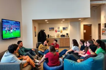 alt_text: A diverse group of teens and young adults socializes in a bright community lounge while watching a sports game on a large TV.